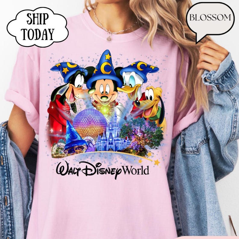 May include: Pink t-shirt featuring Mickey Mouse, Goofy, Donald Duck, and Pluto with a Walt Disney World graphic. The design includes a castle, a sphere, and stars. The shirt has the text "Walt Disney World".