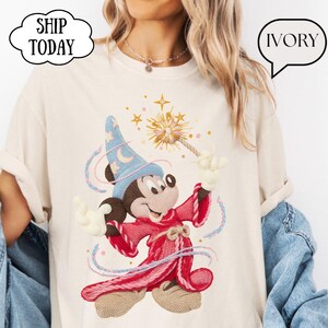 May include: Ivory t-shirt with a cartoon wizard character in a blue hat and red robe, holding a wand with a starburst design. The shirt has the text "SHIP TODAY" in a cloud-shaped speech bubble and "IVORY" in a speech bubble.