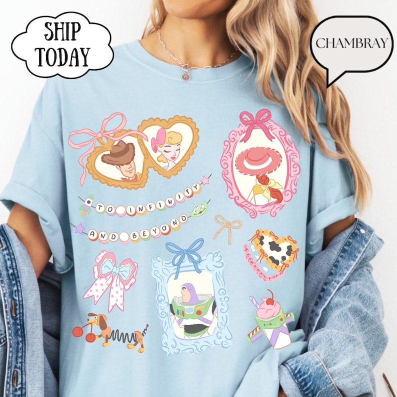 Op de afbeelding: Lichtblauw T-shirt met illustraties van stripfiguren in sierlijke frames. Het shirt bevat de tekst "TO INFINITY AND BEYOND" en de woorden "SHIP TODAY" in een wolk-vormige tekstballon.