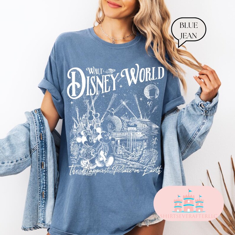 May include: Blue jean-colored t-shirt with a white graphic of Walt Disney World, featuring Mickey Mouse and other characters. The text "Walt Disney World" and "The Happiest Place on Earth" are printed on the front. The shirt is a relaxed fit.
