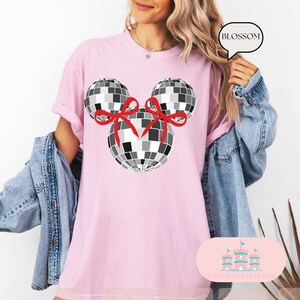 May include: Pink t-shirt featuring a black and white disco ball Mickey Mouse design. The disco balls have red bows on them. The text "BLOSSOM" is in a white speech bubble.