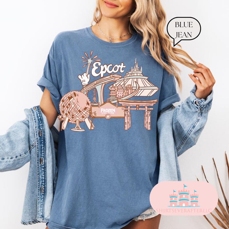 May include: A blue jean t-shirt with a pink and white graphic of Epcot, featuring the Spaceship Earth ride, the World Showcase, and the Frozen Ever After ride. The text "Epcot" is written in a pink font.