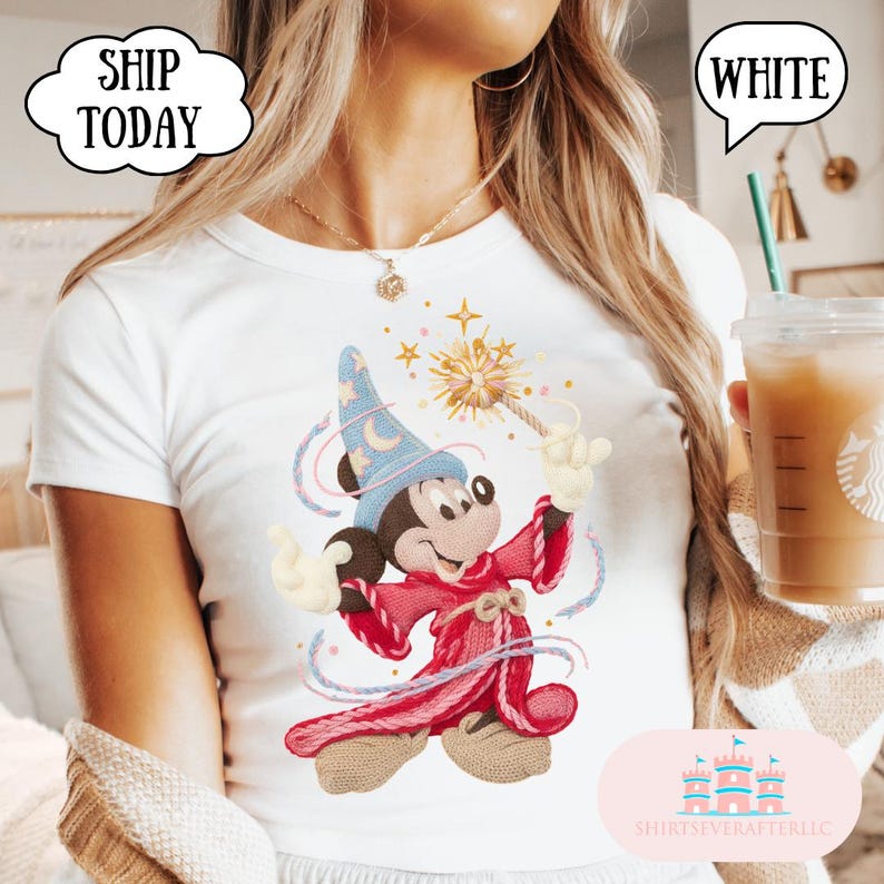 May include: White t-shirt with a colourful illustration of Mickey Mouse as a wizard, holding a magic wand. The design includes a blue wizard hat with a crescent moon, a red robe, and swirling lines. The text "SHIP TODAY" is in a speech bubble.