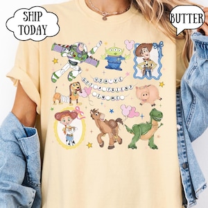 Puede incluir: Una camiseta de color amarillo p&aacute;lido con un estampado gr&aacute;fico de personajes de Toy Story, incluyendo a Buzz Lightyear, un alien&iacute;gena, Woody, Slinky Dog, Hamm, Jessie, Bullseye y Rex, con el texto YOU'VE GOT A FRIEND IN ME en c&iacute;rculo.