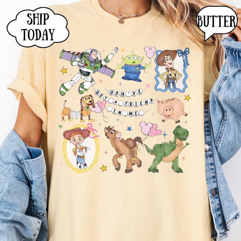 Puede incluir: Una camiseta de color amarillo p&aacute;lido con un estampado gr&aacute;fico de personajes de Toy Story, incluyendo a Buzz Lightyear, un alien&iacute;gena, Woody, Slinky Dog, Hamm, Jessie, Bullseye y Rex, con el texto YOU'VE GOT A FRIEND IN ME en c&iacute;rculo.