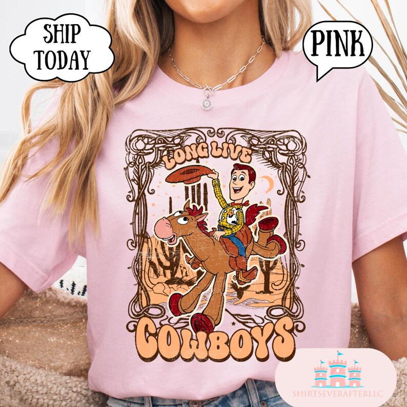 May include: Pink t-shirt featuring a vintage-style graphic of a cowboy riding a horse, with the words "Long Live Cowboys." The design includes a cowboy hat and desert landscape. The shirt is a light pink color.