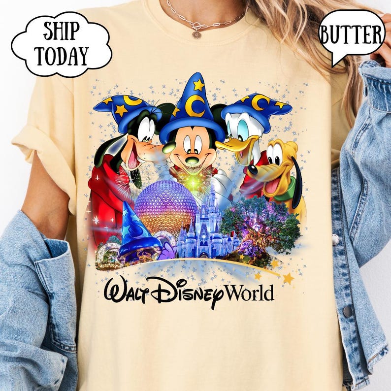 May include: Butter-colored t-shirt featuring a colorful graphic of Mickey Mouse, Goofy, Donald Duck, and Pluto in front of a castle and other Disney World landmarks. The words "Walt Disney World" are printed below the graphic.