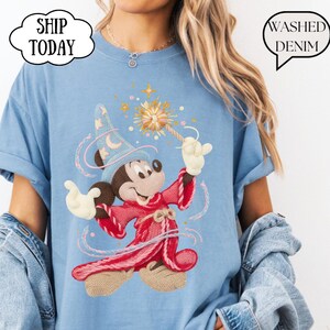 May include: Pale blue t-shirt with a cartoon Mickey Mouse in a wizard outfit, holding a wand with a starburst design. The shirt has the text "Washed Denim" in a speech bubble and "Ship Today" in a cloud-shaped bubble.