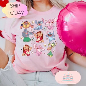 May include: Pink t-shirt with a graphic print of Stitch and other characters from the Disney movie Lilo & Stitch. The shirt has a crew neck and short sleeves.