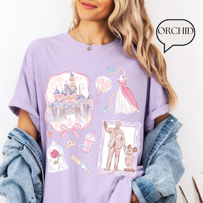 Op de afbeelding: Een lichtpaars T-shirt met verschillende illustraties van een kasteel, jurk, ballonnen en personages. Het woord "ORCHID" staat in een tekstballon. De illustraties zijn in pastelkleuren, wat zorgt voor een grillig en speels ontwerp.