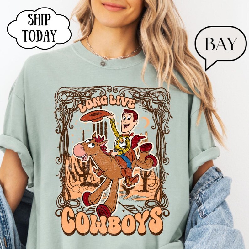 May include: A light green t-shirt featuring a cartoon cowboy riding a horse with the words "Long Live Cowboys". The design includes a cowboy character and a horse in a desert landscape.