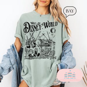 May include: A light green t-shirt featuring a black and white graphic of Walt Disney World with Mickey and Minnie Mouse. The text "Walt Disney World" and "The Happiest Place on Earth" are printed on the shirt.