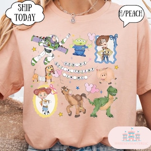 Puede incluir: Una camiseta de color melocot&oacute;n con un estampado gr&aacute;fico de varios personajes animados, incluyendo un ranger espacial, un vaquero, una vaquera, un alien&iacute;gena verde, un dinosaurio, un cerdo, un perro y un caballo, con el texto "YOU'VE GOT A FRIEND IN ME".
