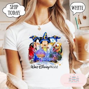 May include: White t-shirt featuring Mickey Mouse, Goofy, Donald Duck, and Pluto with a Walt Disney World graphic. The design includes a castle, a sphere, and stars. The shirt has the text "Walt Disney World".
