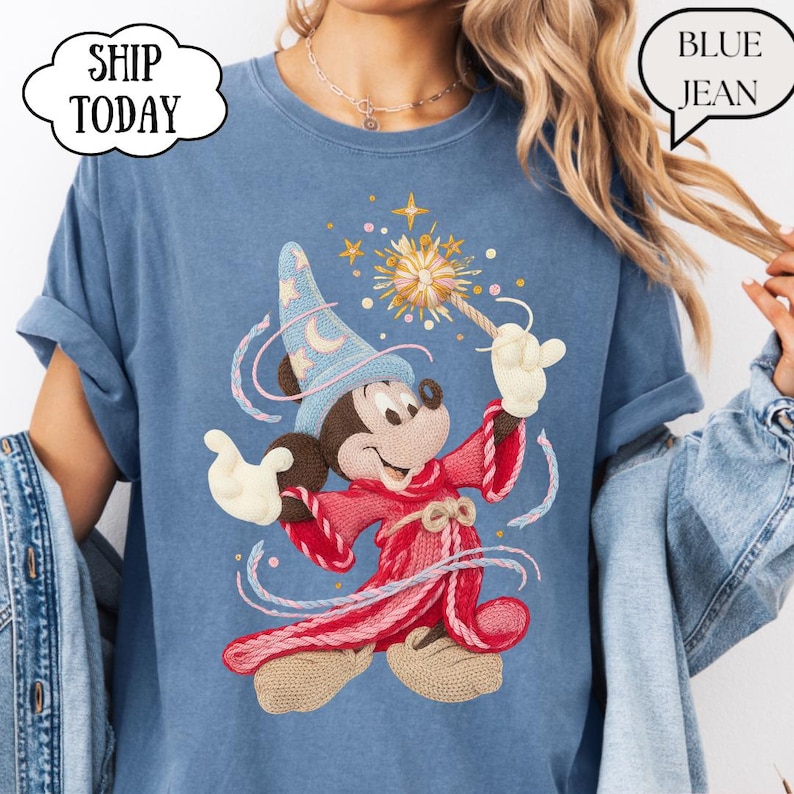 May include: Blue t-shirt with a cartoon wizard Mickey Mouse design. Mickey is wearing a red robe, a blue hat, and holding a magic wand. The shirt has the text "SHIP TODAY" and "BLUE JEAN" in speech bubbles.
