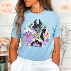 Puede incluir: Una camiseta azul claro con un estampado gr&aacute;fico de cuatro personajes villanos de Disney: Mal&eacute;fica, &Uacute;rsula, la Reina Malvada y Cruella de Vil. Los personajes est&aacute;n rodeados de flores y corazones rotos.