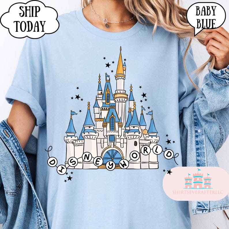 May include: Baby blue t-shirt featuring a detailed illustration of a fairytale castle with blue turrets and gold accents. The text "DISNEY WORLD" is displayed in a circular design. The shirt also has the text "BABY BLUE".