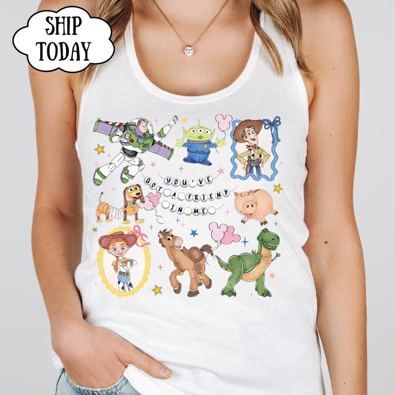 Puede incluir: Una camiseta sin mangas blanca con un estampado gr&aacute;fico colorido de varios personajes animados, incluyendo un ranger espacial, un vaquero, una vaquera, un alien&iacute;gena verde, un dinosaurio, un cerdo y un perro, con el texto "YOU'VE GOT A FRIEND IN ME".