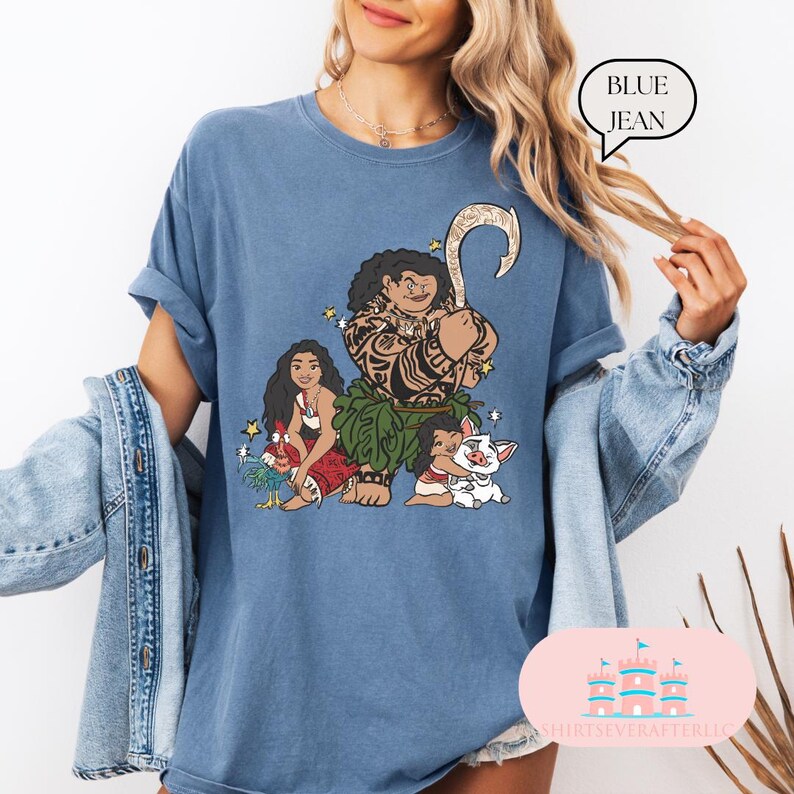 May include: A blue jean t-shirt with a graphic print of Maui, Moana, and Pua from the Disney movie Moana. The graphic shows Maui holding his fish hook, Moana holding a flower, and Pua the pig.