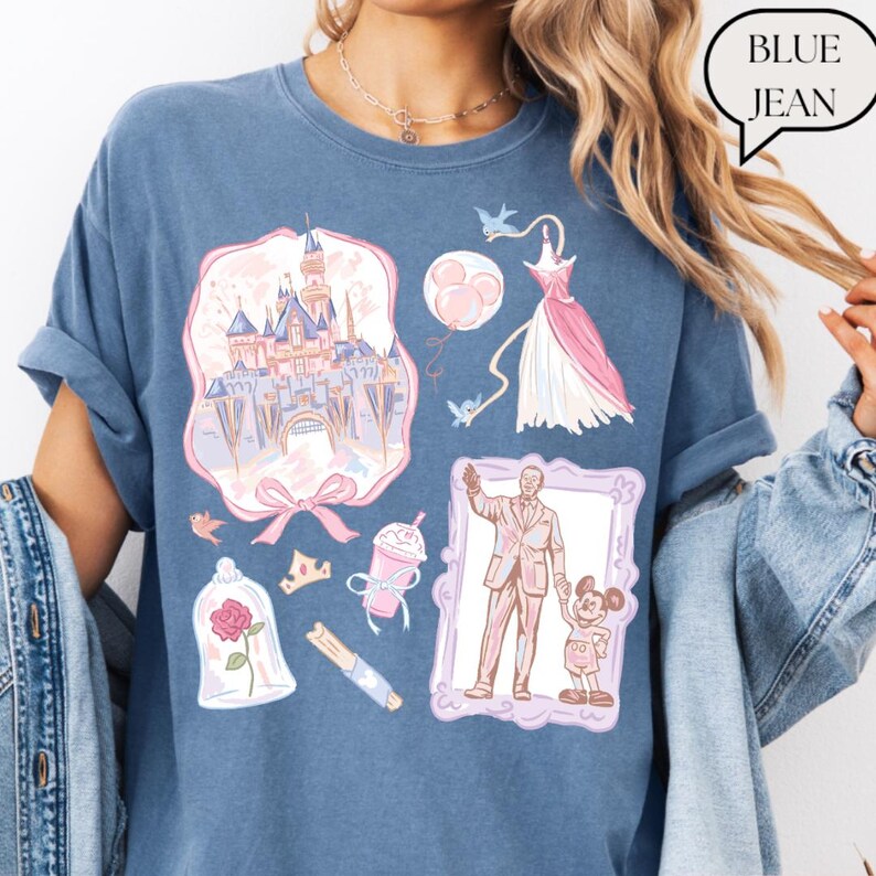 Op de afbeelding: Blauw spijkerbroekkleurig T-shirt met diverse pastelkleurige illustraties. De illustraties omvatten een kasteel, een jurk, een man met een kind, een roos, een kroon en een drankje. De tekst "BLUE JEAN" staat in een tekstballon.