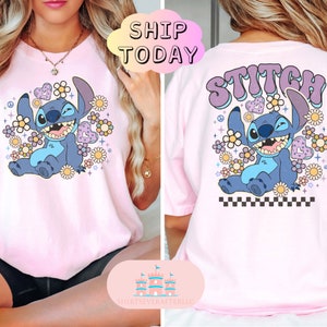 May include: Pink t-shirt with a blue Stitch character from Lilo & Stitch wearing a flower crown and surrounded by flowers. The back of the shirt has the word "Stitch" in a retro font with the same design.
