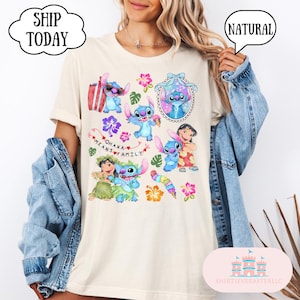 May include: A light beige t-shirt with a colorful graphic print of Stitch characters from the Disney movie Lilo & Stitch. The graphic includes the text "Ohana means family".