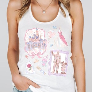 Op de afbeelding: Witte tanktop met diverse pastelkleurige illustraties, waaronder een kasteel, een jurk, ballonnen en een ingelijste afbeelding van een man en een muis. Andere illustraties zijn een roos, een kroon en een drankje.