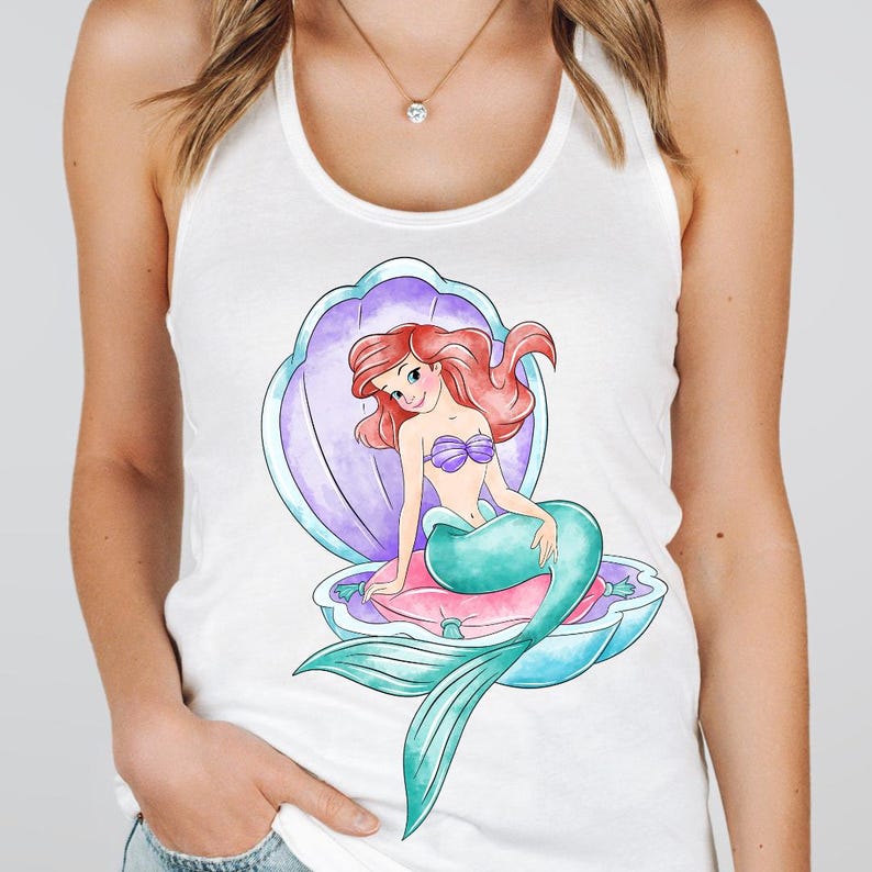 May include: White vest top with a colourful illustration of a mermaid in a seashell. The mermaid has red hair, a purple seashell bra, and a teal tail. The seashell is purple and blue, and the mermaid is sitting on a pink cushion.
