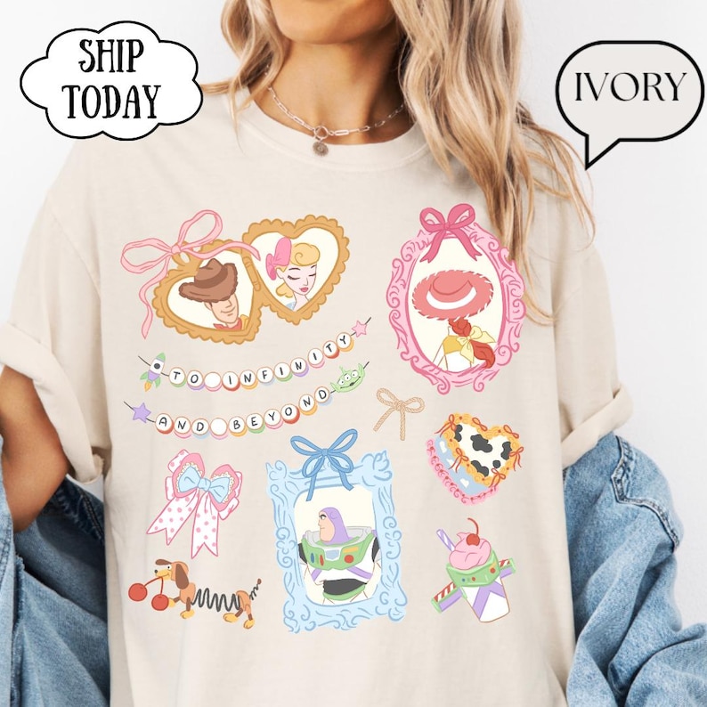 Op de afbeelding: Ivoor kleurig T-shirt met kleurrijke cartoonafbeeldingen van personages en elementen uit een populaire animatiefilm. Het shirt bevat de tekst "TO INFINITY AND BEYOND" en de woorden "SHIP TODAY" en "IVORY" in tekstballonnen.