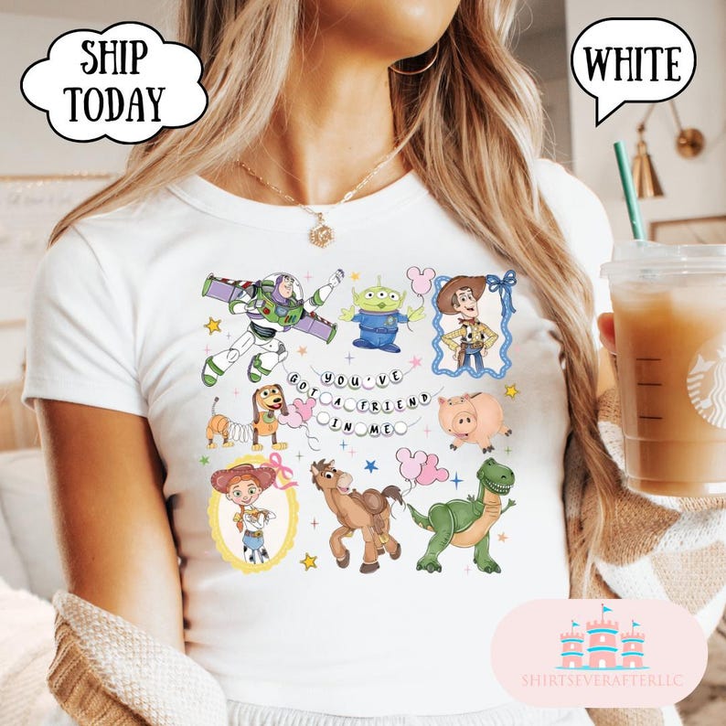Puede incluir: Una camiseta blanca con un estampado gr&aacute;fico colorido de varios personajes animados, incluyendo un ranger espacial, un vaquero, una vaquera, un dinosaurio verde, un cerdo, un perro con cuerpo de muelle y un alien&iacute;gena, con el texto "YOU'VE GOT A FRIEND IN ME".