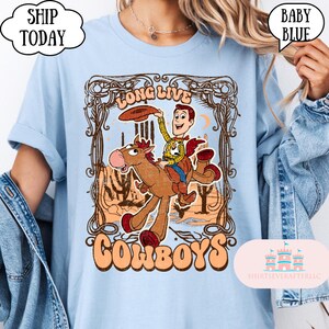 May include: Baby blue t-shirt with a graphic featuring a cowboy riding a horse, with the words "LONG LIVE COWBOYS". The design includes a cartoon cowboy character and a desert landscape.