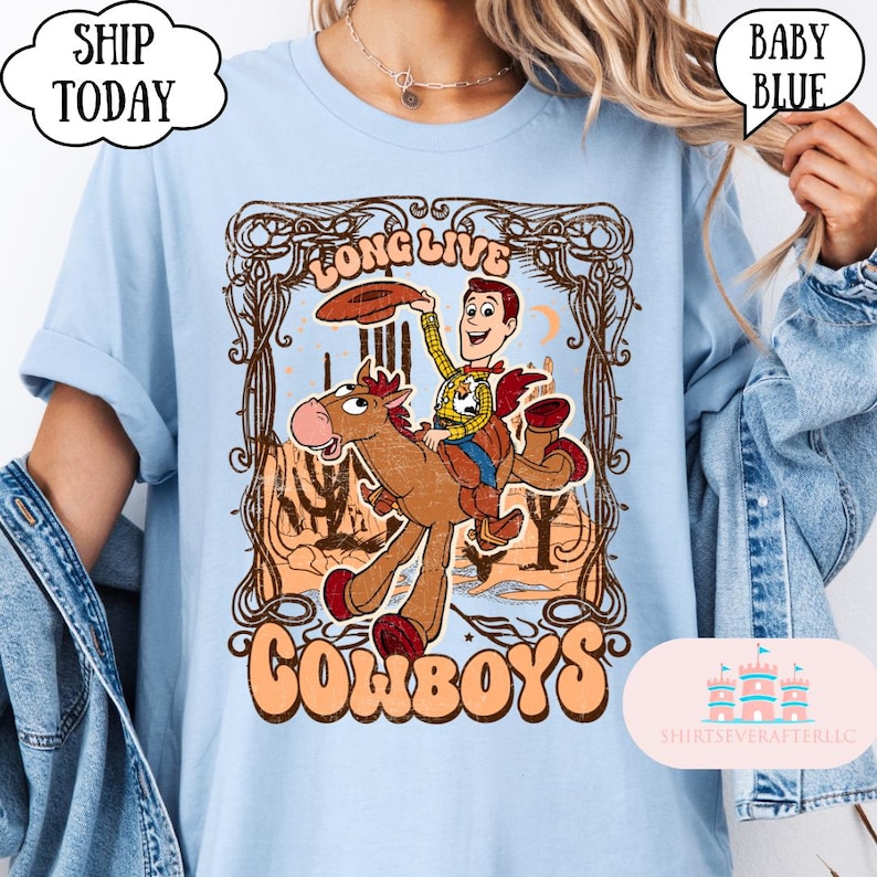 May include: Baby blue t-shirt with a graphic featuring a cowboy riding a horse, with the words "LONG LIVE COWBOYS". The design includes a cartoon cowboy character and a desert landscape.