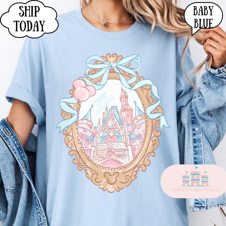 Puede incluir: Camiseta azul beb&eacute; con una ilustraci&oacute;n enmarcada en oro de un castillo de cuento de hadas con detalles en rosa y azul. El dise&ntilde;o incluye un lazo y globos. El texto en la camiseta dice "BABY BLUE" y "SHIP TODAY".