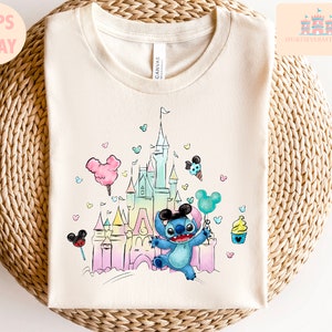 May include: A light blue Stitch character holding a balloon in front of a pastel pink and blue watercolor illustration of Cinderella's castle. The background is filled with small hearts and Mickey Mouse ears.