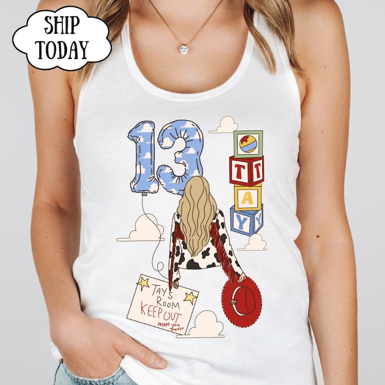 May include: A white tank top featuring a graphic of a person with long blonde hair wearing a cow-print jacket with red fringe. The design includes a blue cloud-patterned number 13 balloon, stacked alphabet blocks, and a sign reading Tays Room Keep Out.