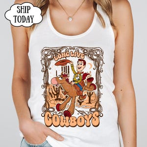 May include: White tank top featuring a cartoon illustration of a cowboy riding a horse. The design includes the text "Long Live Cowboys" and "Ship Today". The cowboy is holding a hat, and the horse is brown with red hooves.