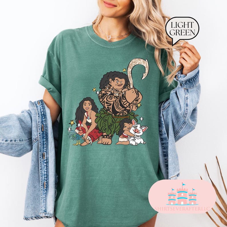 May include: A green t-shirt with a graphic print of Maui, Moana, and Pua from the Disney movie Moana. The characters are depicted in their signature poses and attire.