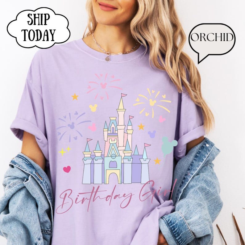 May include: A lilac t-shirt with a castle graphic, fireworks, and stars. The words "Birthday Girl" are in cursive. The shirt also has the text "SHIP TODAY" and "ORCHID" in speech bubbles.