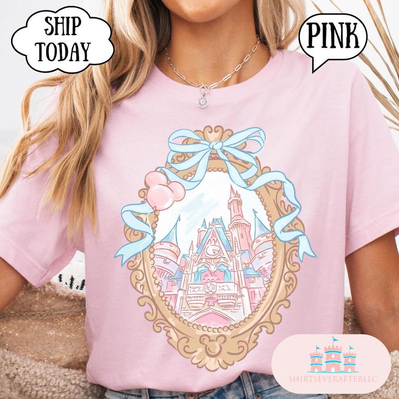 Puede incluir: Camiseta rosa claro con una ilustraci&oacute;n enmarcada en oro de un castillo de cuento de hadas con detalles azules y globos rosas. La camiseta tiene la palabra "PINK" en un bocadillo.