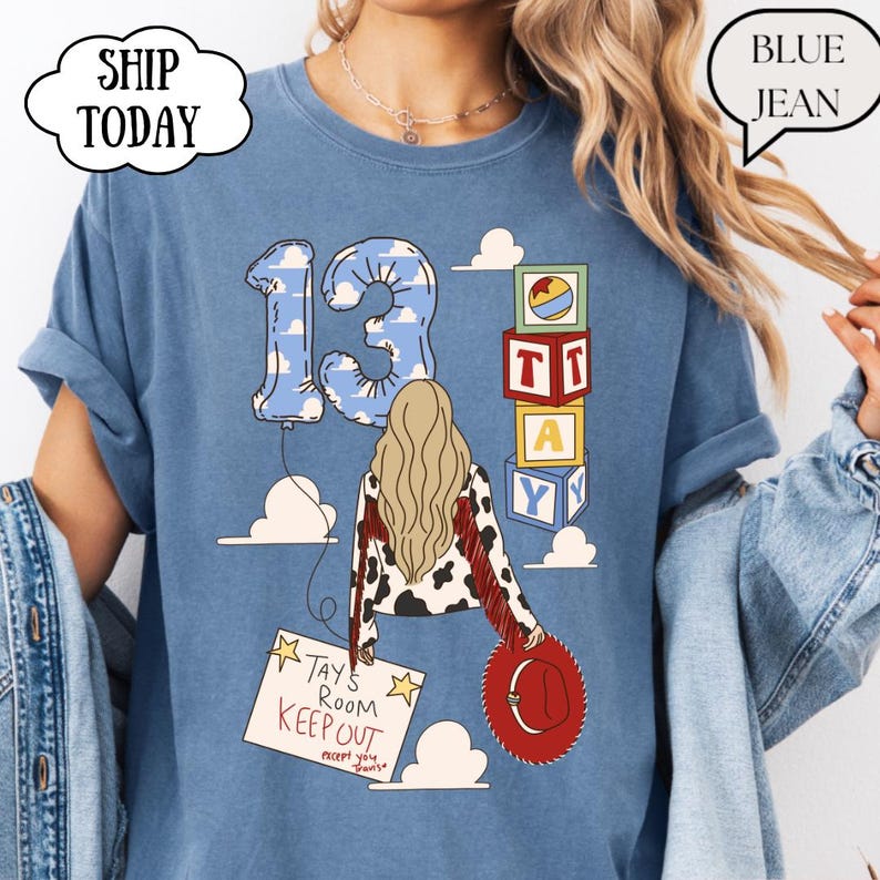 May include: A blue t-shirt featuring a graphic of a person with long blonde hair wearing a cow-print jacket with red fringe. The design includes a number 13 balloon, stacked alphabet blocks, a red cowboy hat, and a sign reading Tays Room Keep Out.