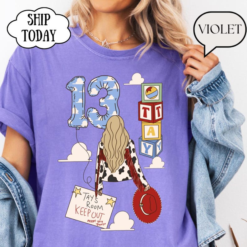 May include: A violet t-shirt featuring a graphic of a person with blonde hair wearing a cow-print jacket with red fringe, holding a red hat. The design includes a number 13 balloon, stacked alphabet blocks spelling TAY, and a sign reading TAY'S ROOM KEEP OUT.
