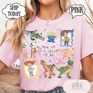 Puede incluir: Una camiseta rosa claro con un estampado gr&aacute;fico de varios personajes de Toy Story, incluidos Buzz Lightyear, Woody, Jessie, Slinky Dog, Rex, Hamm y un Alien. El texto "YOU'VE GOT A FRIEND IN ME" aparece en el centro con peque&ntilde;as estrellas.