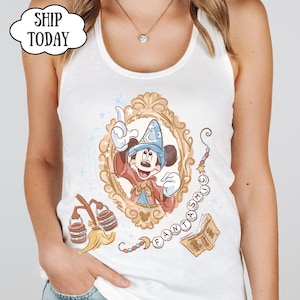 K&ouml;nnte beinhalten: Wei&szlig;es Tanktop mit einer gerahmten Illustration von Mickey Mouse in einem Zauberer-Outfit. Das Design enth&auml;lt das Wort "FANTASMIC" und andere magische Elemente. Das Top hat einen Rundhalsausschnitt und ist &auml;rmellos.