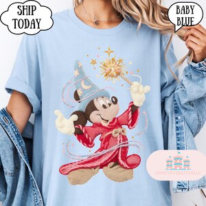May include: Pale blue t-shirt with an embroidered Mickey Mouse design as a sorcerer, holding a wand with stars. The shirt has the text "SHIP TODAY" and "BABY BLUE" in speech bubbles. The brand name "SHIRTSEVERAFTERLLC" is also visible.
