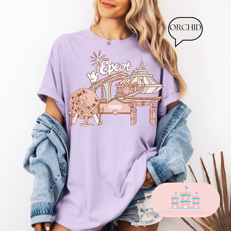 May include: A lavender t-shirt featuring a graphic of Epcot, a theme park in Orlando, Florida. The graphic includes the iconic Spaceship Earth, the Test Track ride, and the Frozen Ever After ride. The text "Epcot" is written in a retro font.
