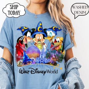 May include: Light blue t-shirt featuring Mickey Mouse, Donald Duck, Goofy, and Pluto with a castle and the text "Walt Disney World." The shirt has a "Washed Denim" graphic.