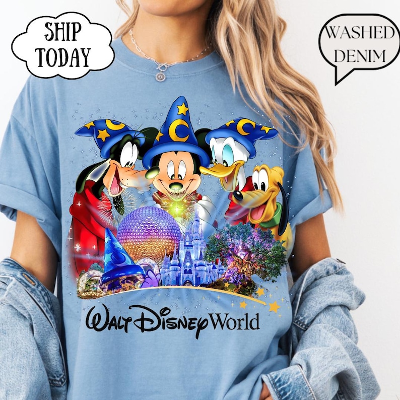 May include: Light blue t-shirt featuring Mickey Mouse, Donald Duck, Goofy, and Pluto with a castle and the text "Walt Disney World." The shirt has a "Washed Denim" graphic.