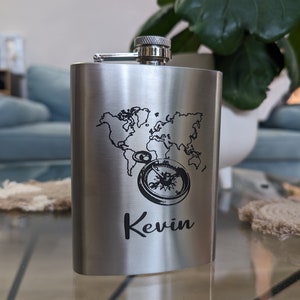 May include: A silver flask featuring a world map and compass design. The flask is engraved with the name "Kevin".