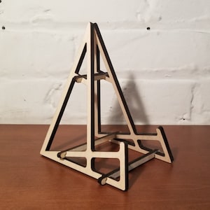 Op de afbeelding: Een houten displaystandaard met een driehoekige vorm en een donkerbruine afwerking. De standaard is gemaakt van multiplex en heeft een eenvoudig, modern ontwerp.