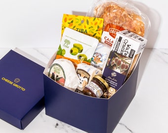 May include: A blue gift box filled with a gourmet cheese and snack gift set. The box contains two rounds of cheese, crackers, olives, chocolate, and a jar of honey. The box is labeled "Cheese Grotto".